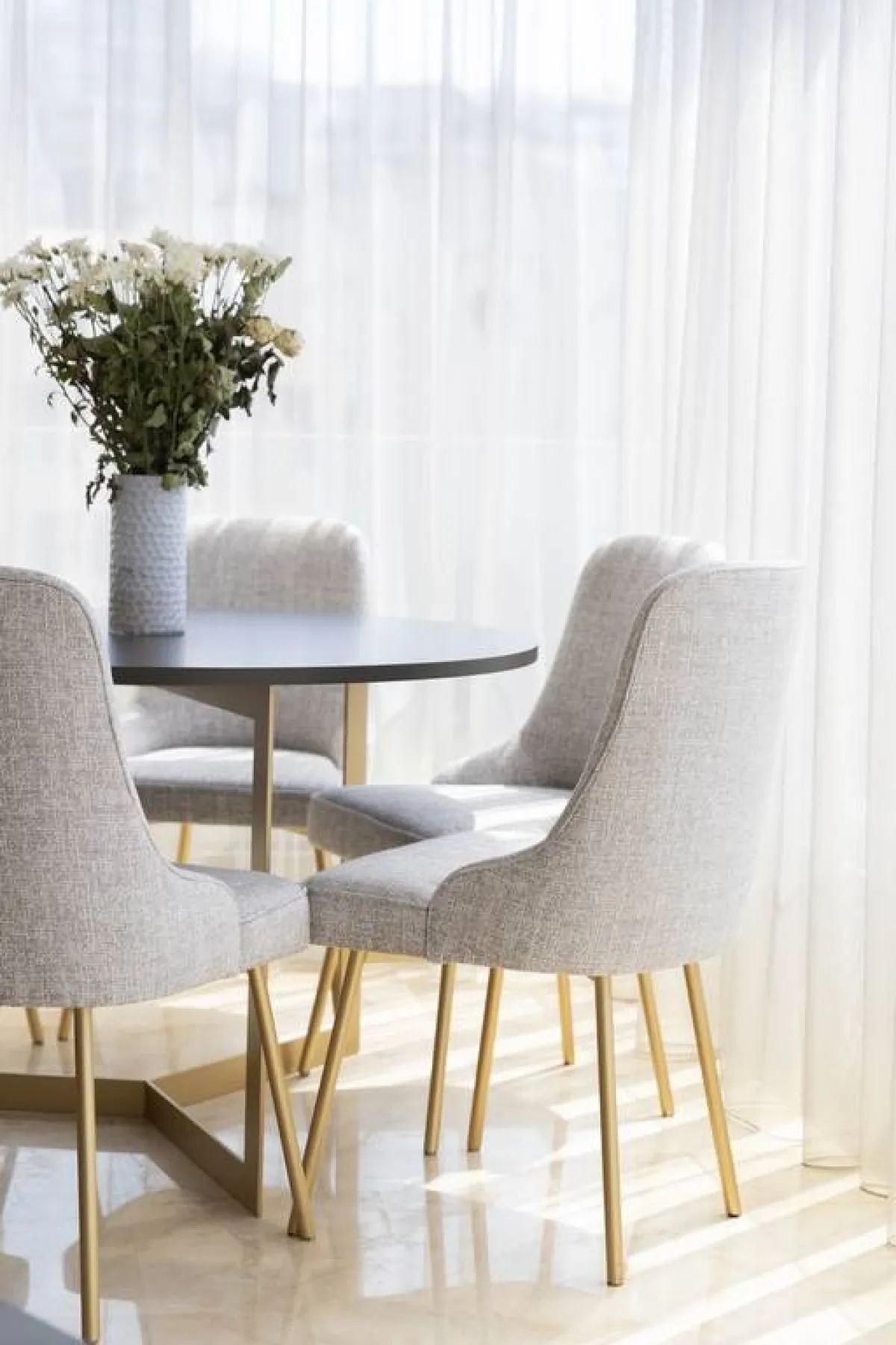 الغرفة مظلّلة بستائر ترشح الضوء الآتي من النوافذ الضخمة