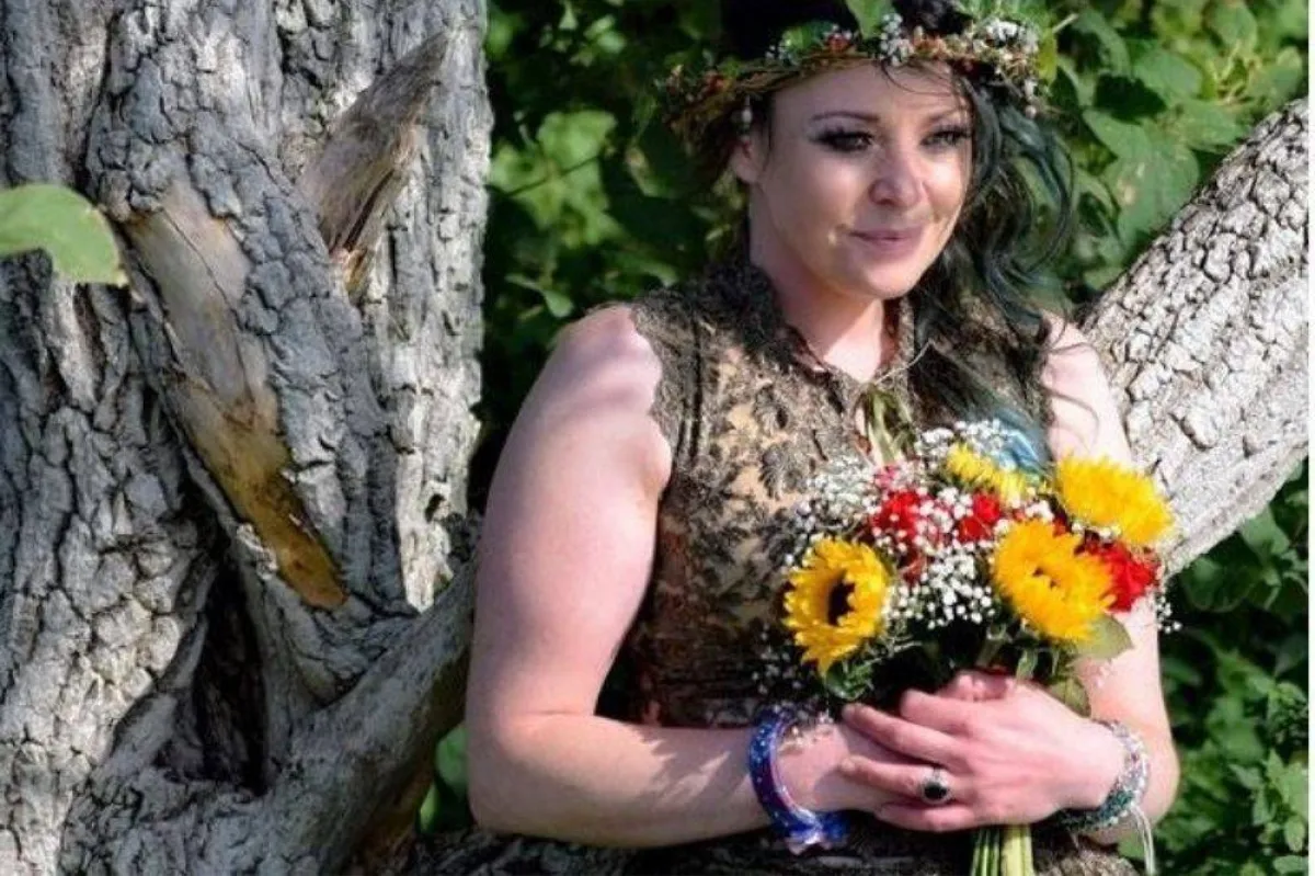 سيدة تحمل زهورا وتقف أمام شجرة