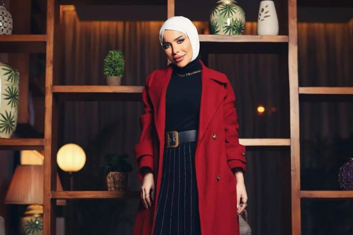 زهراء أشكناني بتنورة بليسيه طويلة ومعطف أحمر داكن مع إيشارب أبيض 
