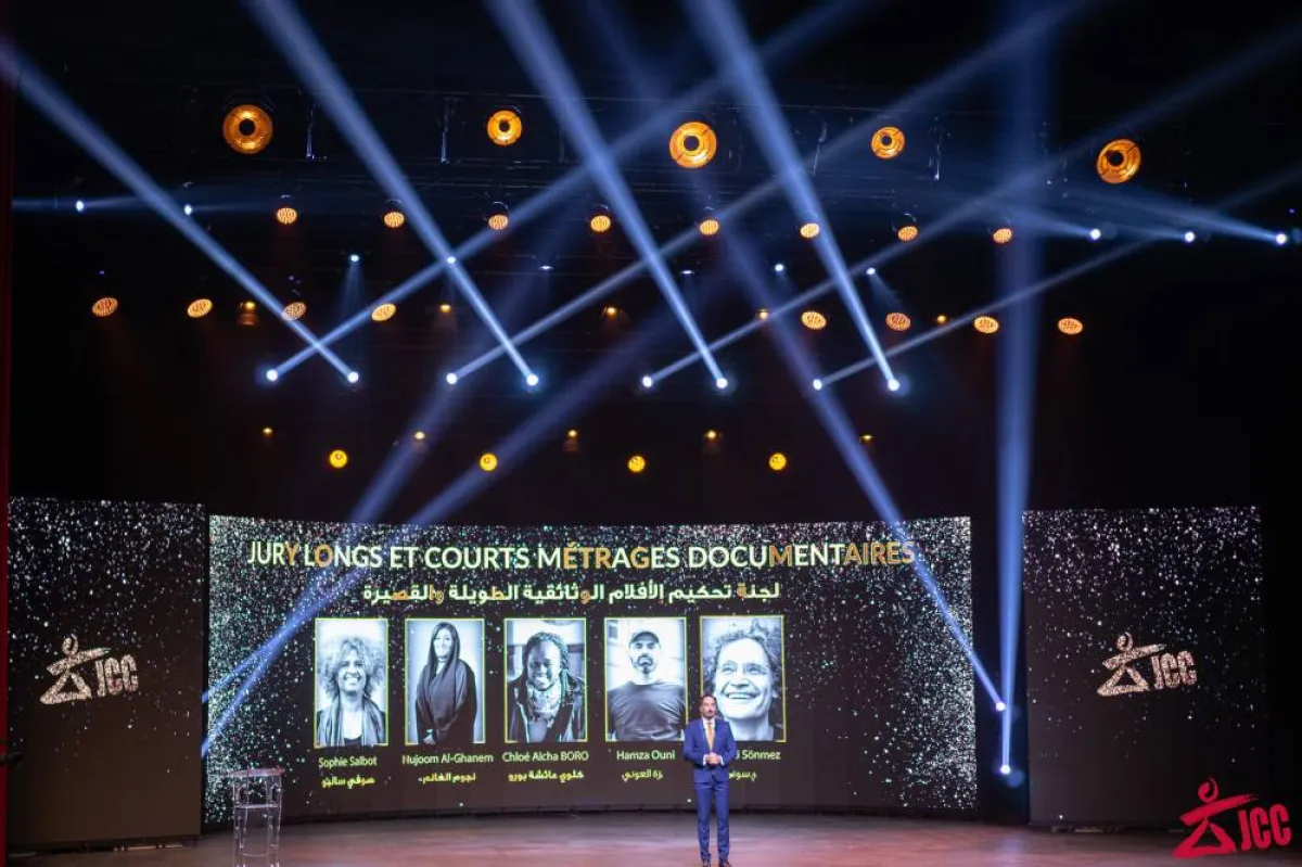 مقدم حفل الاختتام نجيب بلقاضي وخلفه شاشة عملاقة تظهر صور وأسماء أعضاء لجنة تحكيم الأفلام الوثائقية -الصورة من موقع المهرجان