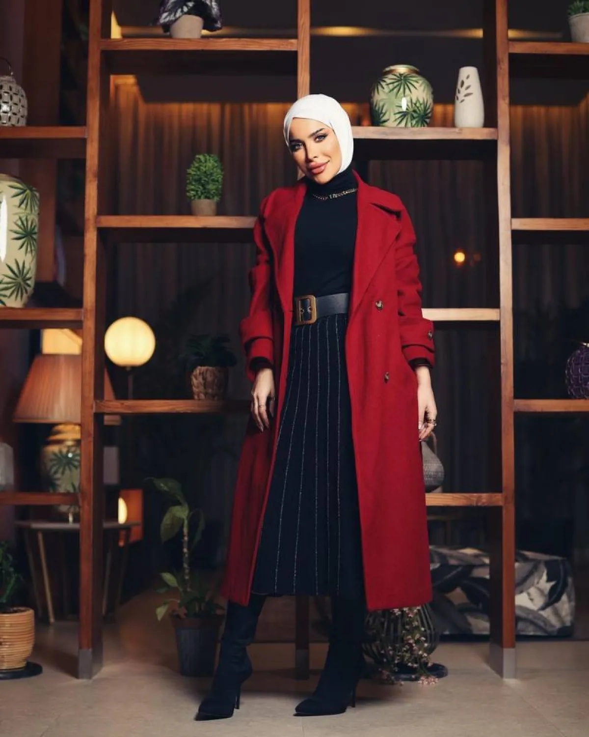 زهراء أشكناني بتنورة بليسيه طويلة ومعطف أحمر داكن مع إيشارب أبيض 