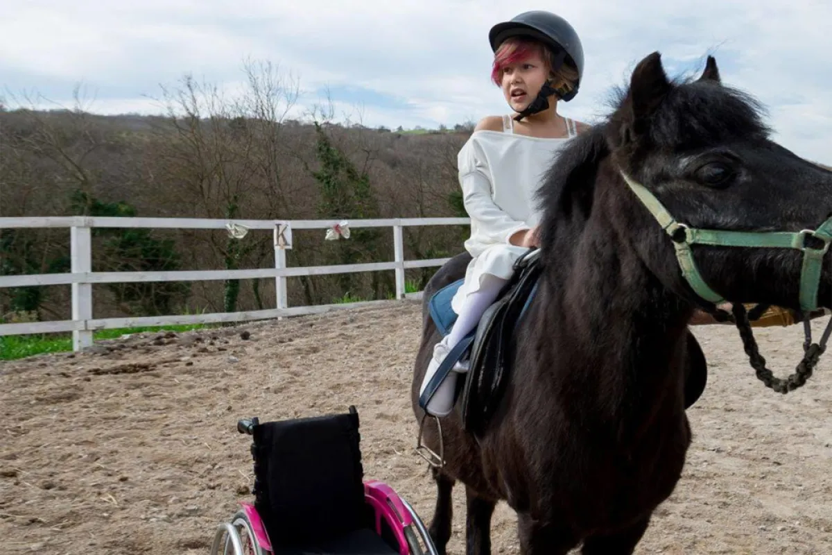 صورة لطفلة من ذوي الهمم تمتطي جواداً