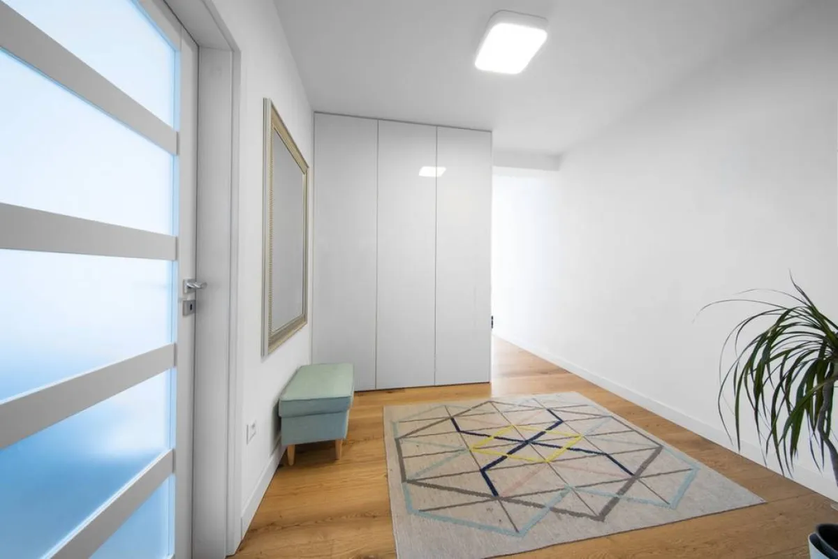 سجادة تفترش أرضيّة الممرّ الداخلي البسيط، الذي يتضمّن مقعدًا مدمجة وظيفة التخزين به، تعلوه مرآة