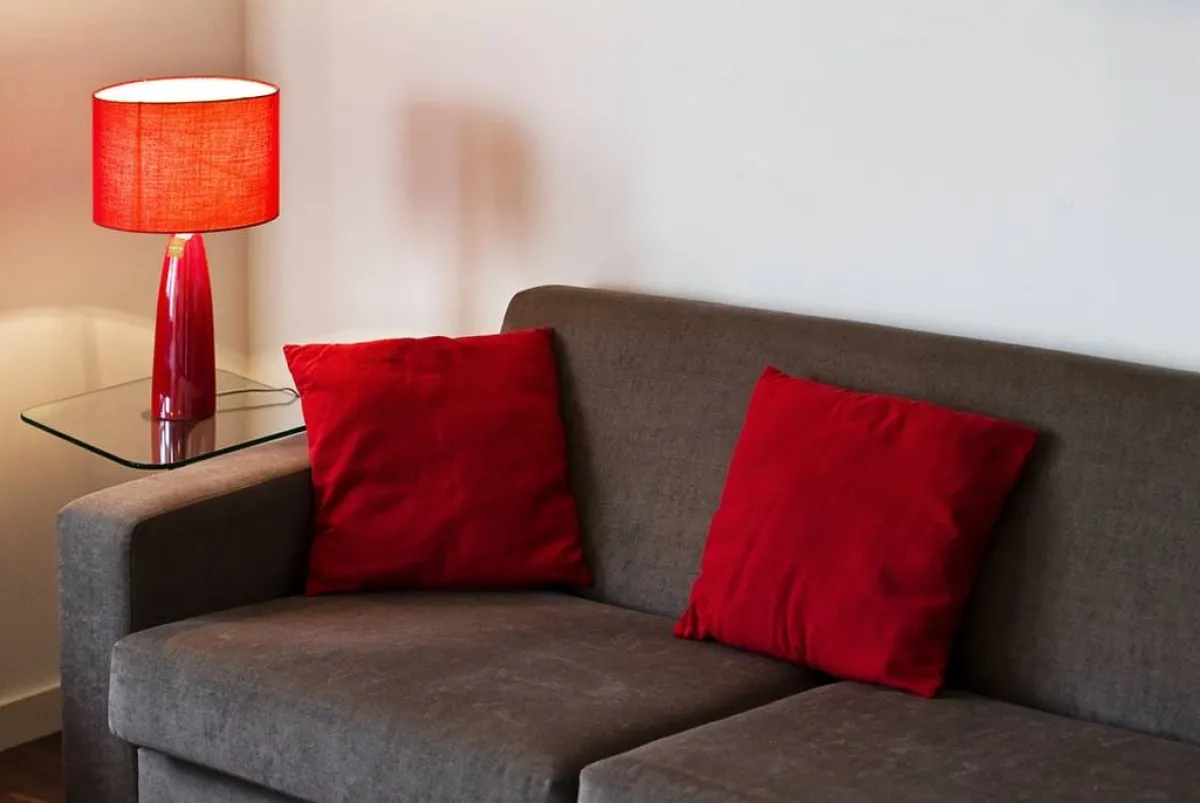 اللون الأحمر يبدو في ديكورات غرفة المعيشة عن طريق زوجي الوسائد والإضاءة الجانبيّة