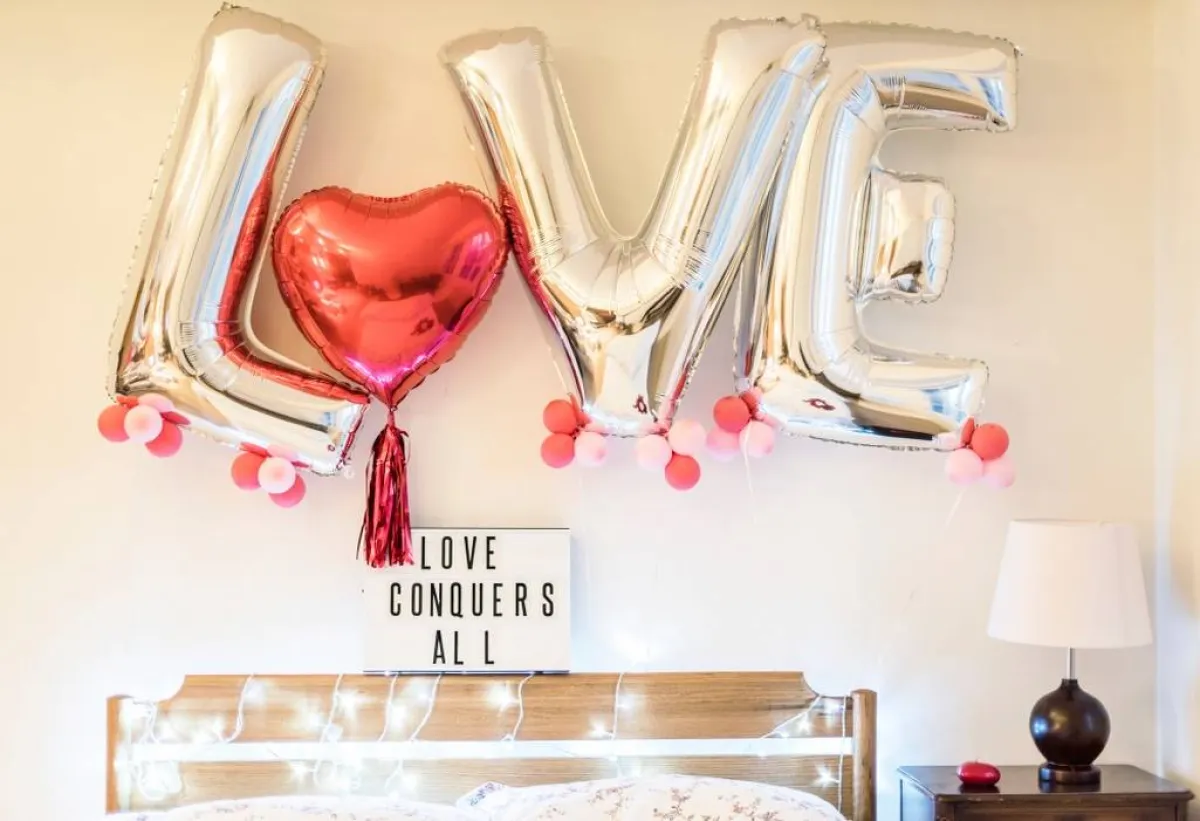 إضاءة وبالونات ولافتة محملة بعبارة رومانسيّة، في غرفة النوم، لمناسبة يوم الحبّ