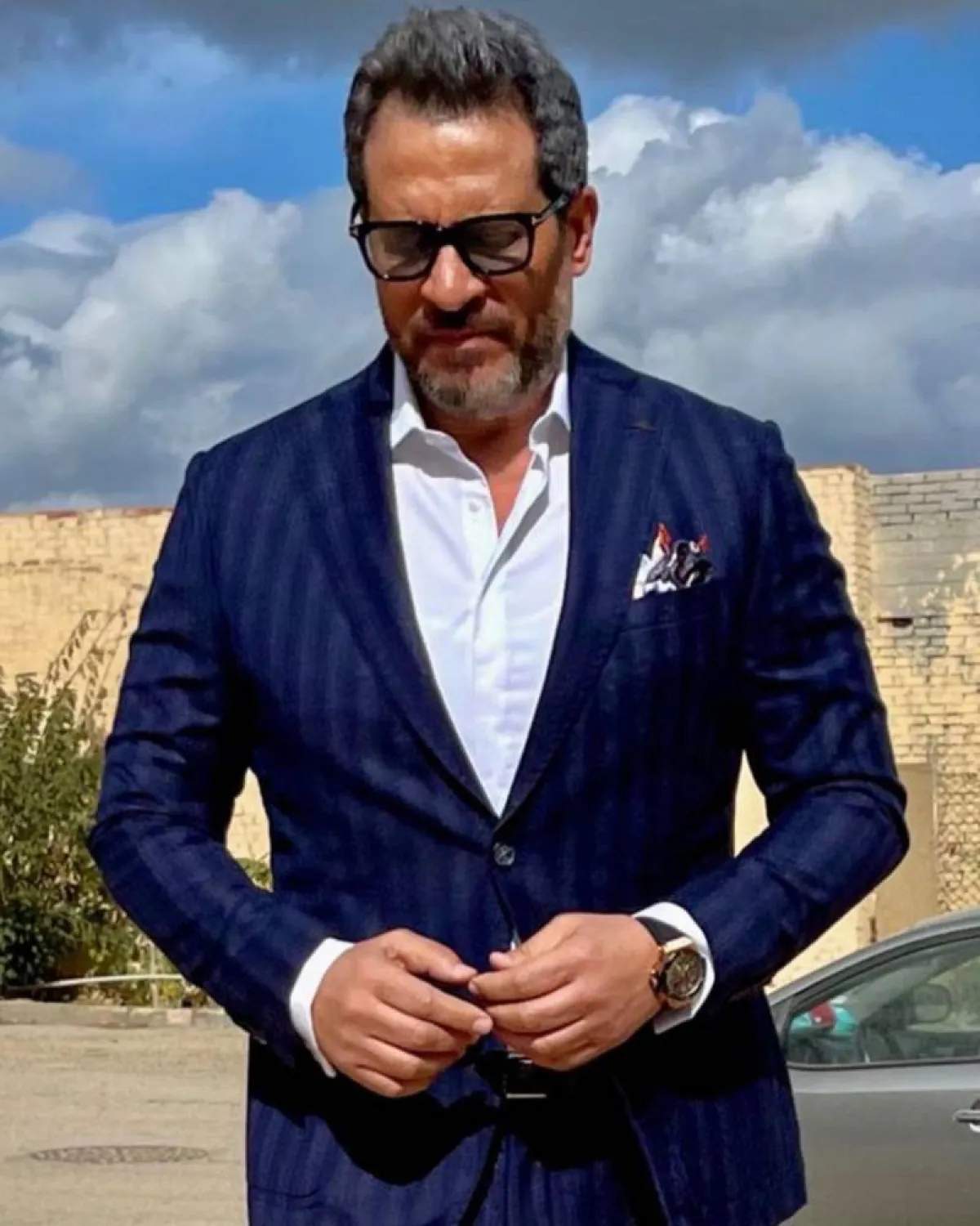 ماجد المصري ببليزر أزرق وقميص أبيض ومنديل جيب بالألوان الأسود والأبيض والأحمر