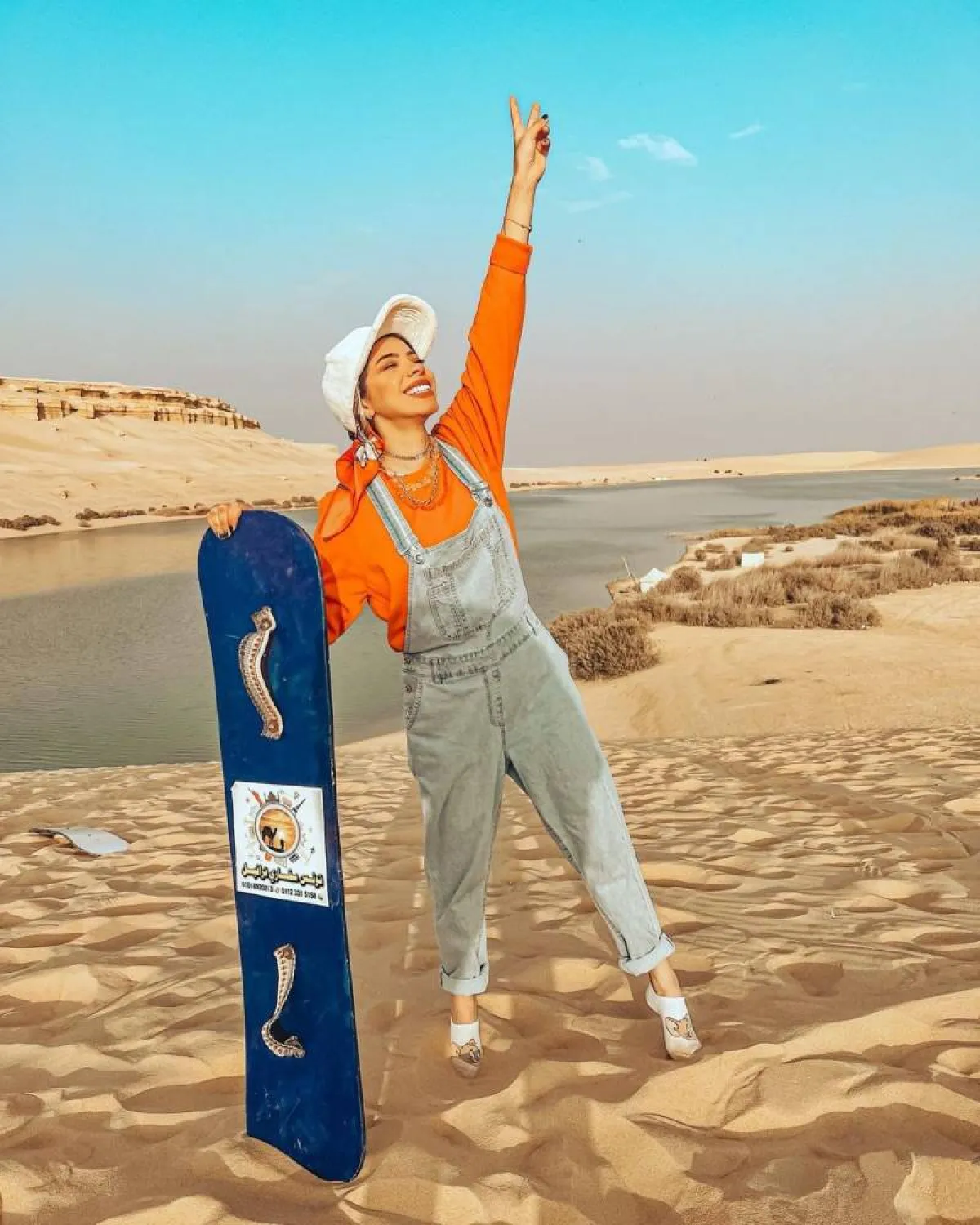 منة السُني بجمبسوت من الجينز وقبعة باللون الأبيض