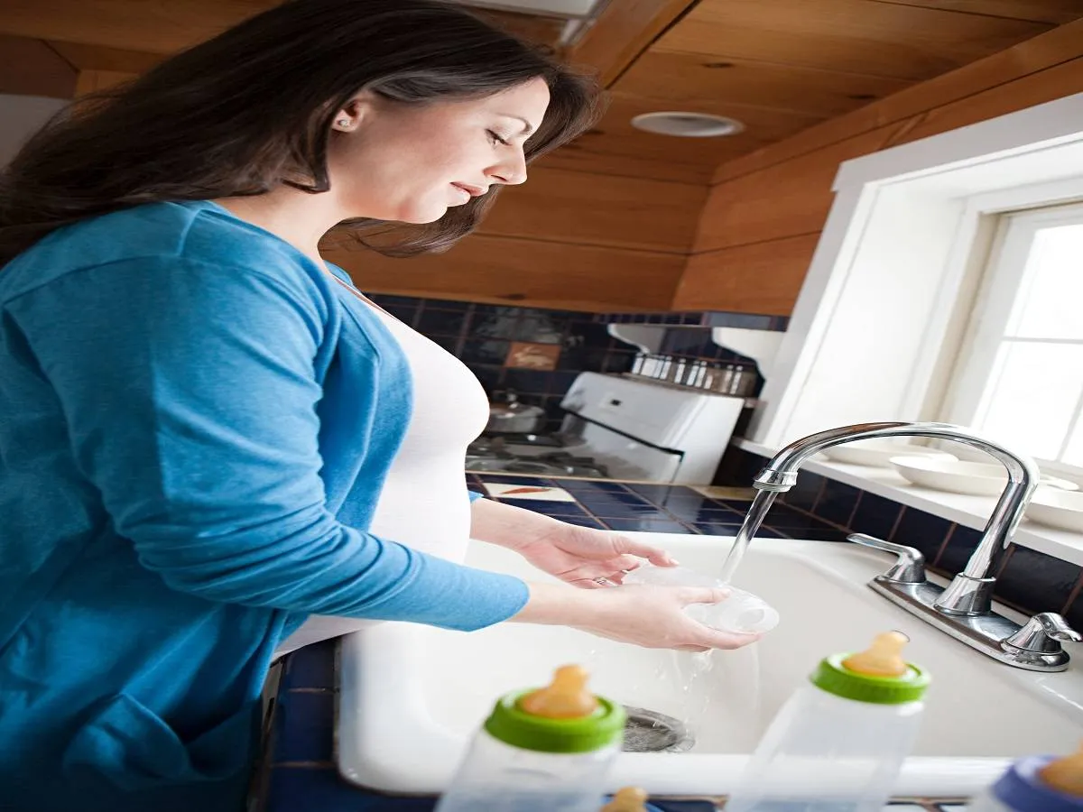 صورة لحامل تقوم بغسل زجاجة حليب صناعي