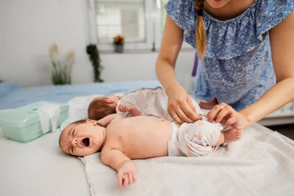 صورة لأم تقوم بتغيير ملابس التوأم الخاصة بهما