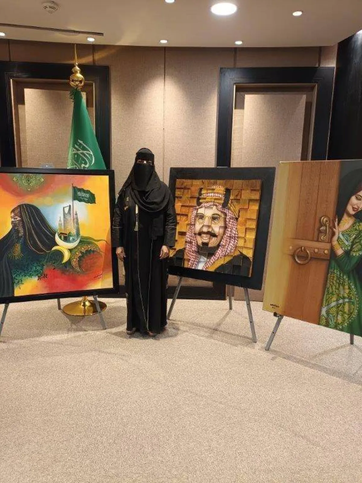 الفنانة التشكيلية منيرة السليم إلى جانب لوحاتها التي تحاكي الوطن