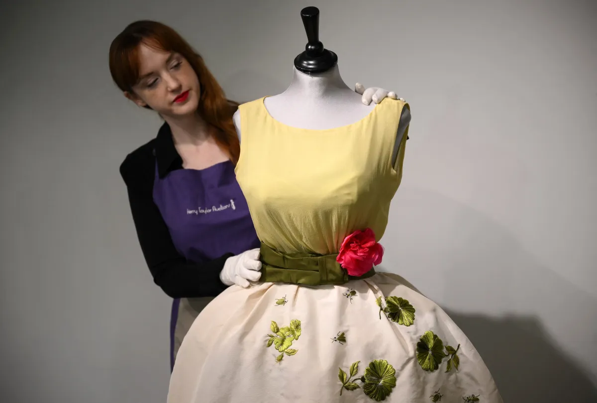An employee poses with a Christian Dior dress worn by actress Elizabeth Taylor, and recently discovered with other dresses in a suitcase, ahead of their sale at Kerry Taylor Auctions, in London on November 25, 2022. A "lucky charm" Christian Dior dress worn by Elizabeth Taylor on the night she won best actress at the 1961 Oscars is to be sold at auction on December 6, 2022, after being stored in a suitcase in London for over 50 years.Daniel LEAL / AFP