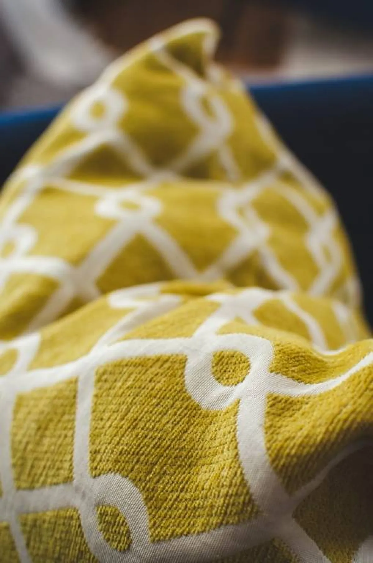 وسادة ذات نسيج باللون الأصفر الخردلي في الخلفيّة، مع نقوش بيض