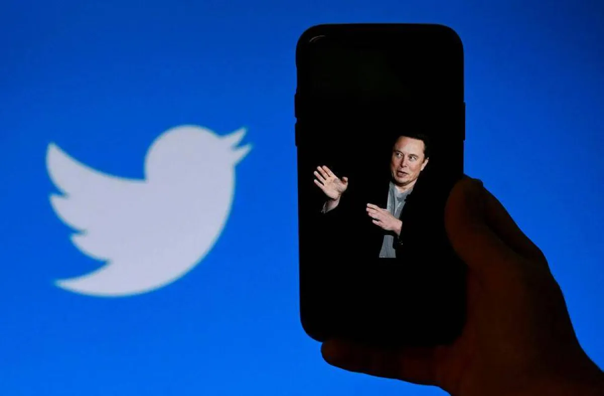 In this photo illustration, a phone screen displays a photo of Elon Musk with the Twitter logo shown in the background, on October 4, 2022, in Washington, DC. Elon Musk has offered to push through with his buyout of Twitter at the original agreed price, reports said Tuesday, prompting a surge in the share price of the social network that triggered a suspension of trading. OLIVIER DOULIERY / AFP