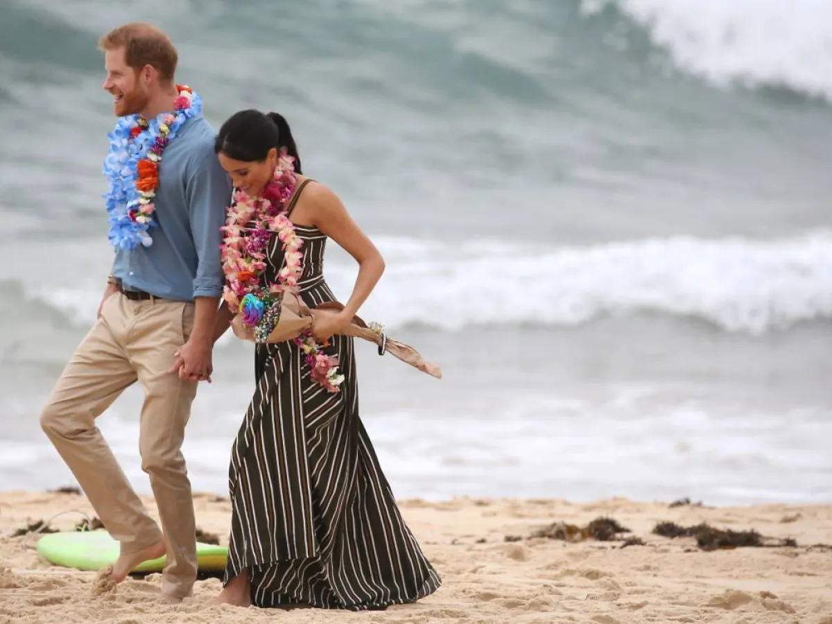 Britain's Prince Harry walks with his wife Meghan, Duchess of Sussex as they meet the local community at Bondi Beach in Sydney on October 19, 2018. British royals Harry and Meghan kicked off their shoes and donned tropical garlands on October 19, as they hit Sydney's famed Bondi beach for the latest stop on their Australian tour. DAVID MOIR / AFP