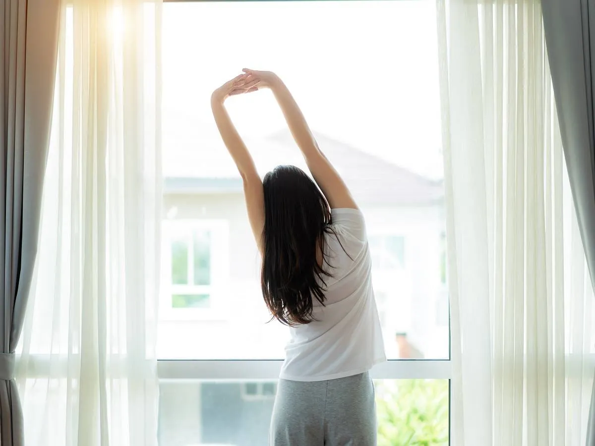 صورة لامرأة تقف أمام نافذة في الصباح