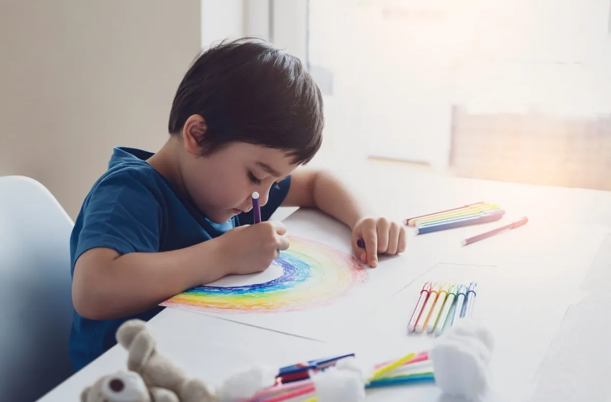 صورة لطفل مشغول بالرسم وحوله الألوان