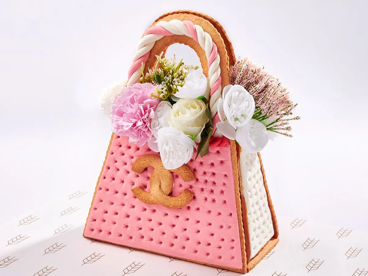 قالب حلوى على شكل حقيبة باللون الوردي ومزينة بالزهور الطبيعية