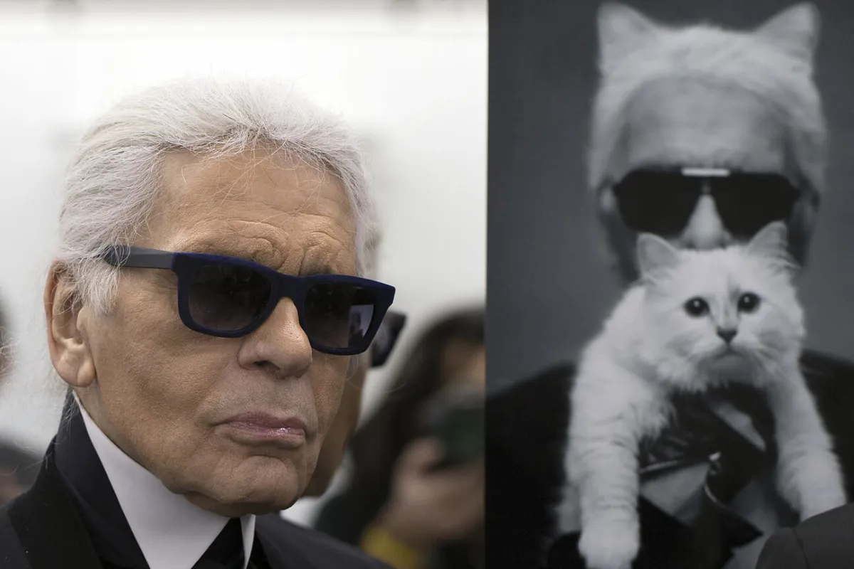 Karl Lagerfeld poses next to a photo of himself and his cat Choupette during a visit to the workshops that work for Chanel in Pantin, outside of Paris, on February 7, 2014. PHOTO / JOEL SAGET Joël SAGET / AFP