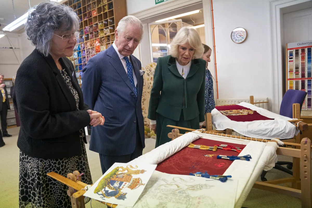King Charles III (C) and the Britain's Camilla, Queen Consort (R) look at their throne seat covers during a visit to the Royal College of Needlework at Hampton Court Palace in East Molesey, south-west London on March 21, 2023. Kirsty O'Connor / POOL / AFP