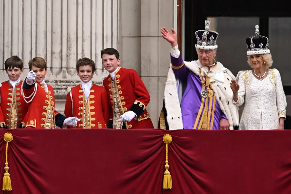 King Charles III wearing the Imperial state Crown, and Britain's Queen Camilla wearing a modified version of Queen Mary's Crown, flanked by Britain's Prince George of Wales (2nd L) and other pages of honour, wave from the Buckingham Palace balcony after viewing the Royal Air Force fly-past in central London on May 6, 2023, after their coronations. Oli SCARFF / AFP