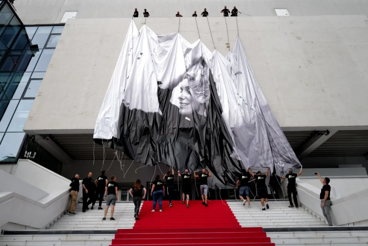 Workers set up the official poster of the 76th Cannes Film Festival on the facade of the Palais des Festivals, in Cannes, southeastern France, on May 14, 2023. Cannes Film festival will take place from May 16 to May 27. (Photo by Valery HACHE / AFP)