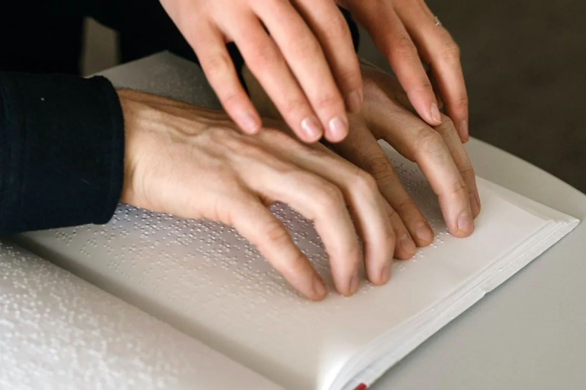 أصابع شخص يلمس شخص آخر يقرأ بطريقة برايل 