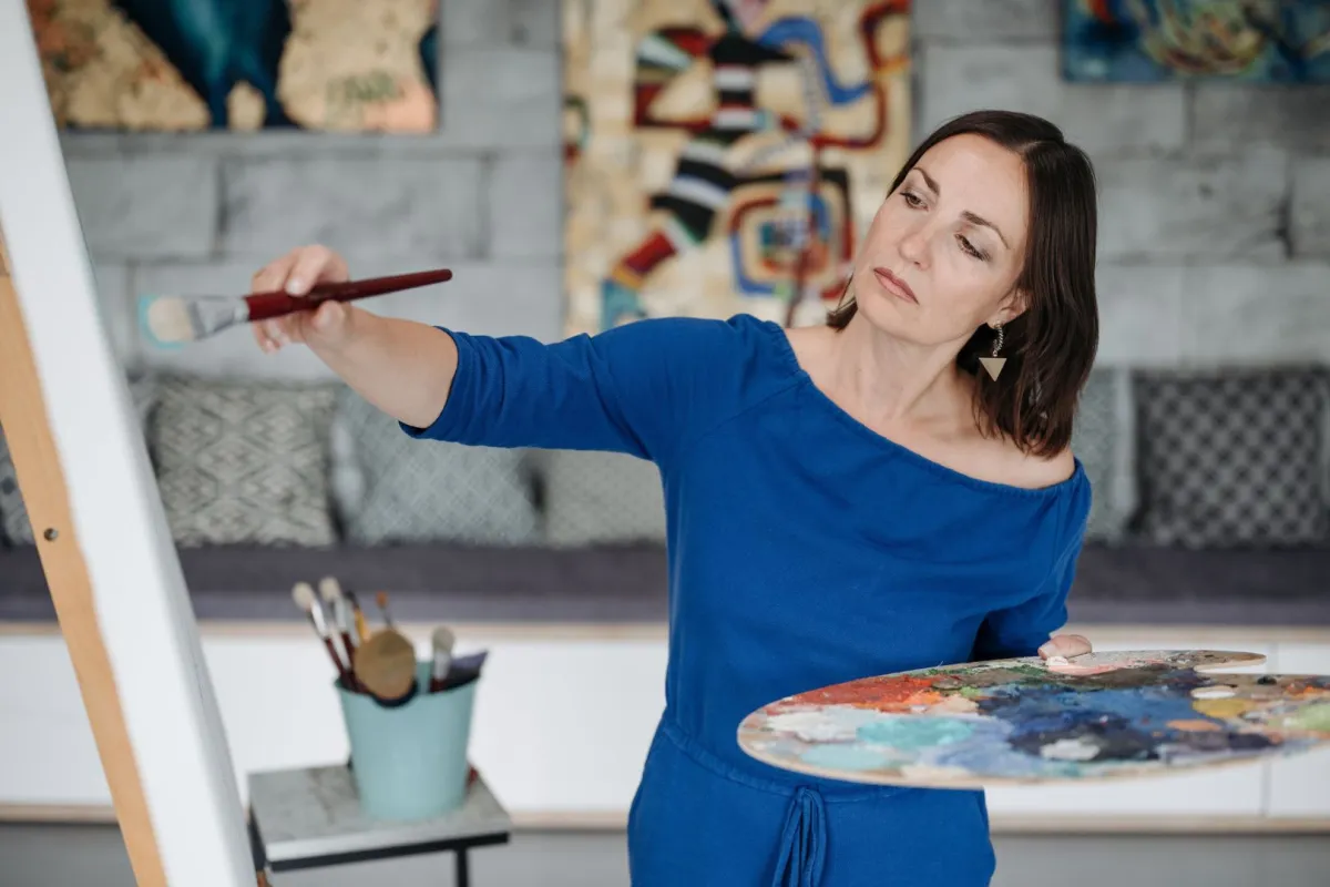 فنانة تشكيلية ترتدي فستاناً أزرق ترسم لوحة  في المرسم