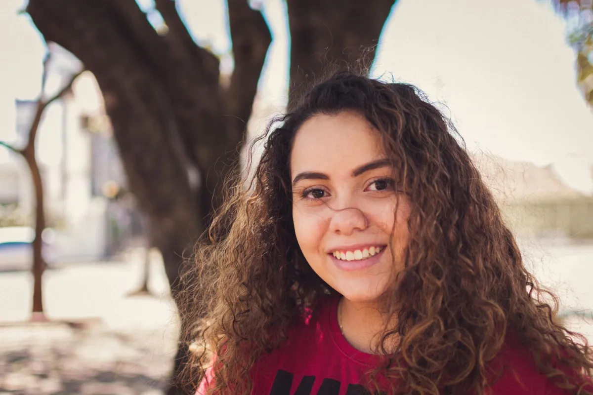 فتاة تبتسم في سعادة تقف ويبدو وراءها جذع شجرة