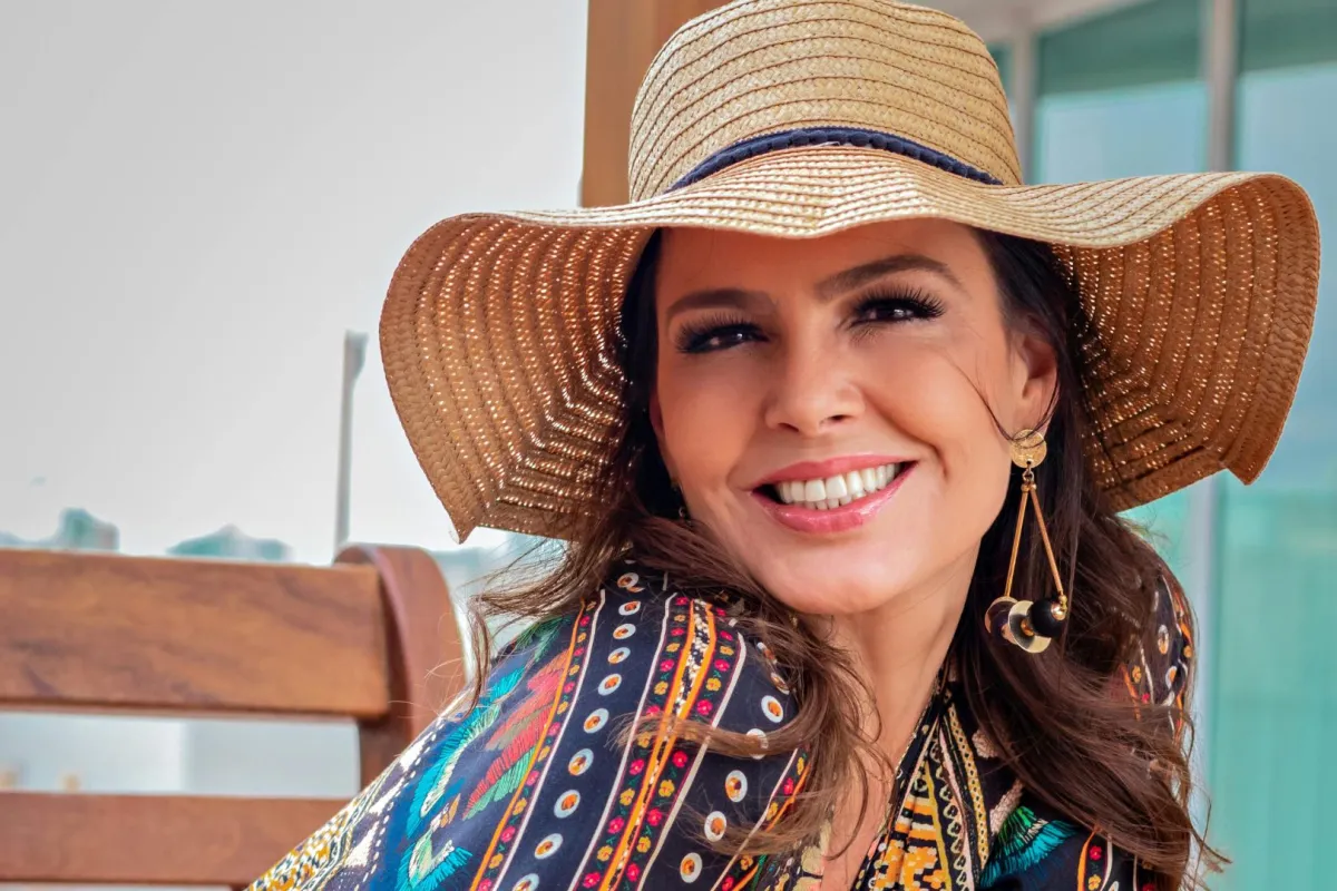 فتاة باسمة ترتدي قبعة من الخوص وتبتسم بسعادة وهي جالسة على مقعد خشبي