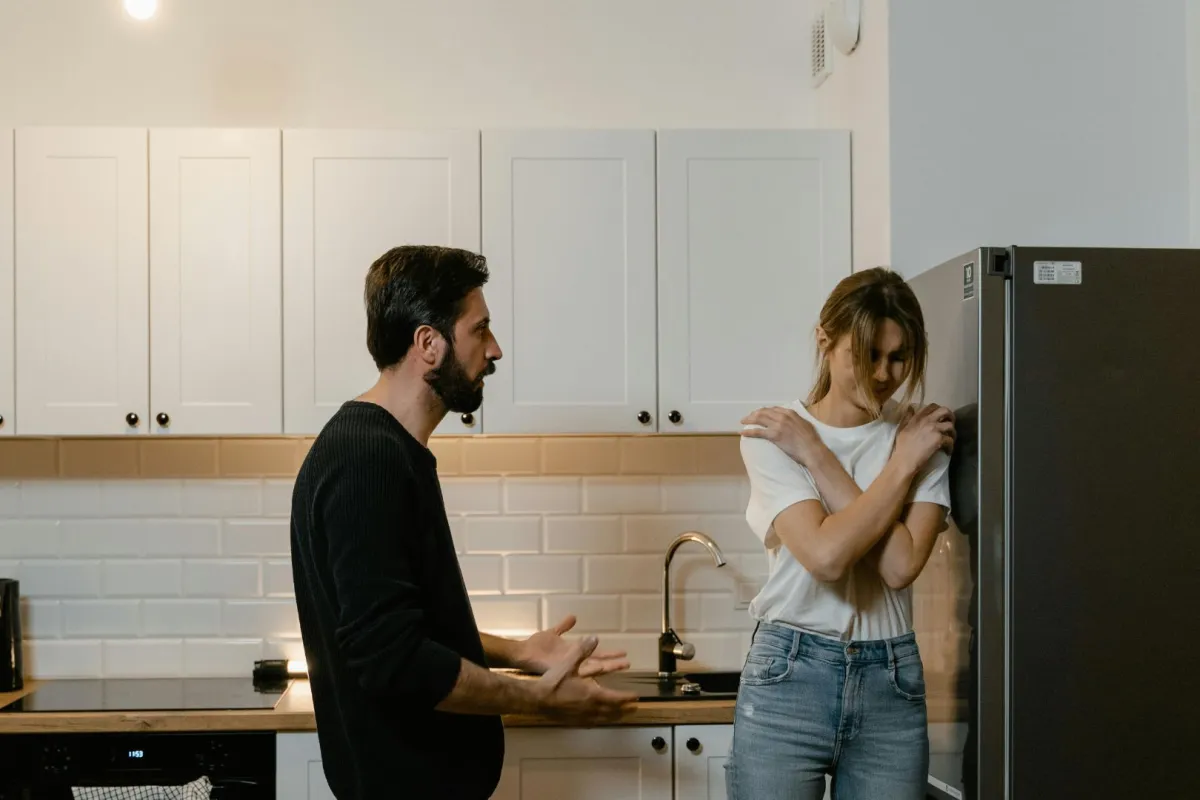  زوجة شابة معنفة تحاول أن تبرر تصرفاتها أمام زوجها المتسلط الذي يقف امامها محاولا تهدئتها