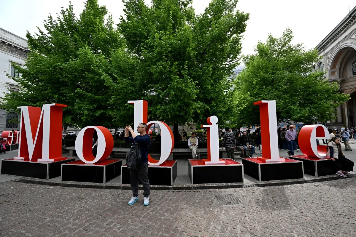 People stand next to a sign promoting the Salone del Mobile (furniture fair) on the eve of the Milan Design Week, on April 15, 2024 in Milan. (Photo by GABRIEL BOUYS / AFP)