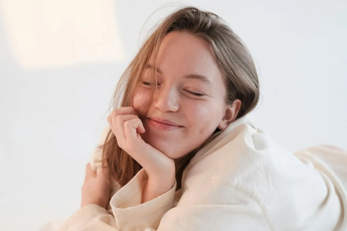 فتاة تبتسم بكسل وهي ترتدي رداء النوم وتظهر أشعة الشمس منعكسة على أحد الجدران