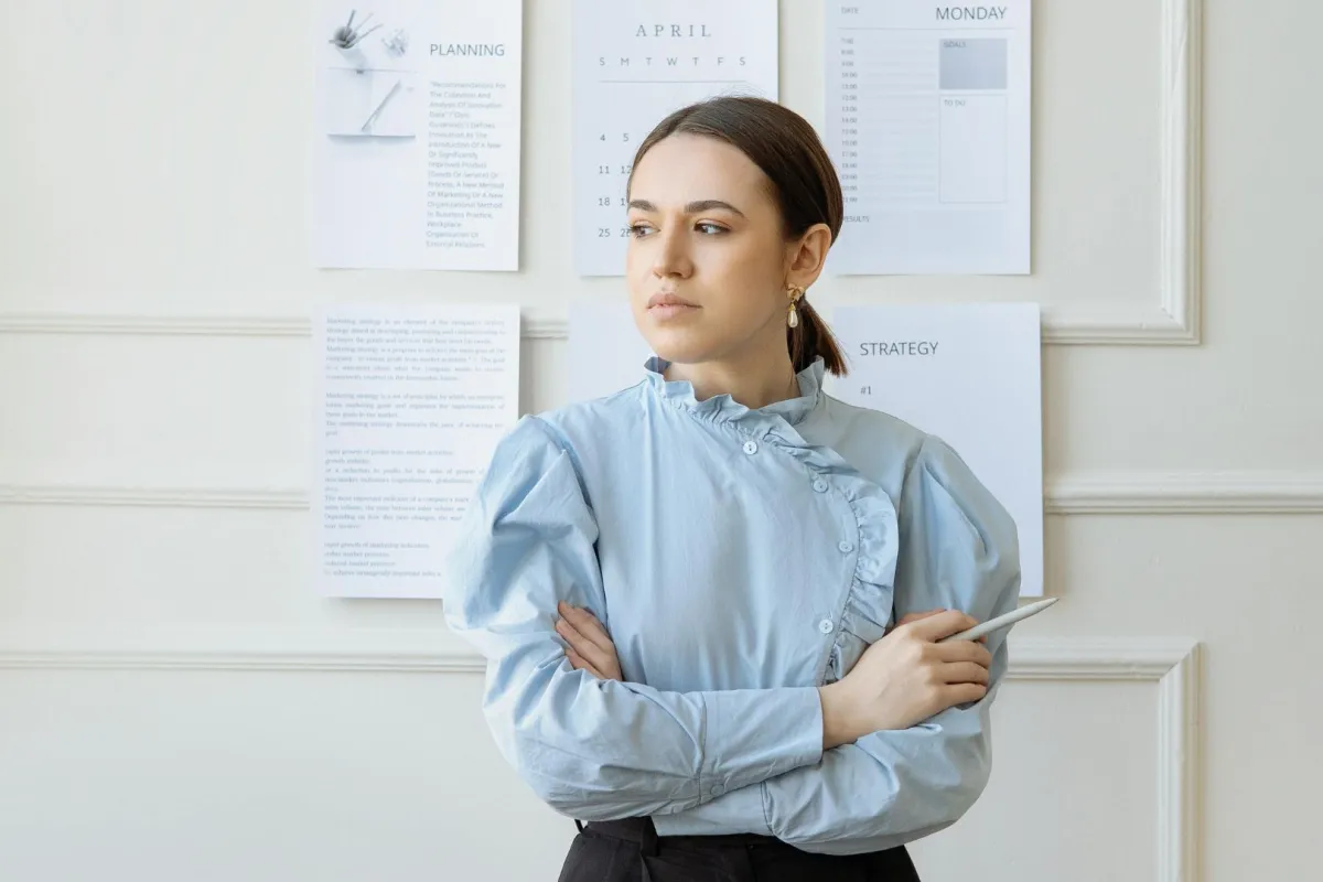 فتاة تقف أمام حائط ملصق عليه بعض الاوراق وتضع يديها حول بعضهما البعض 