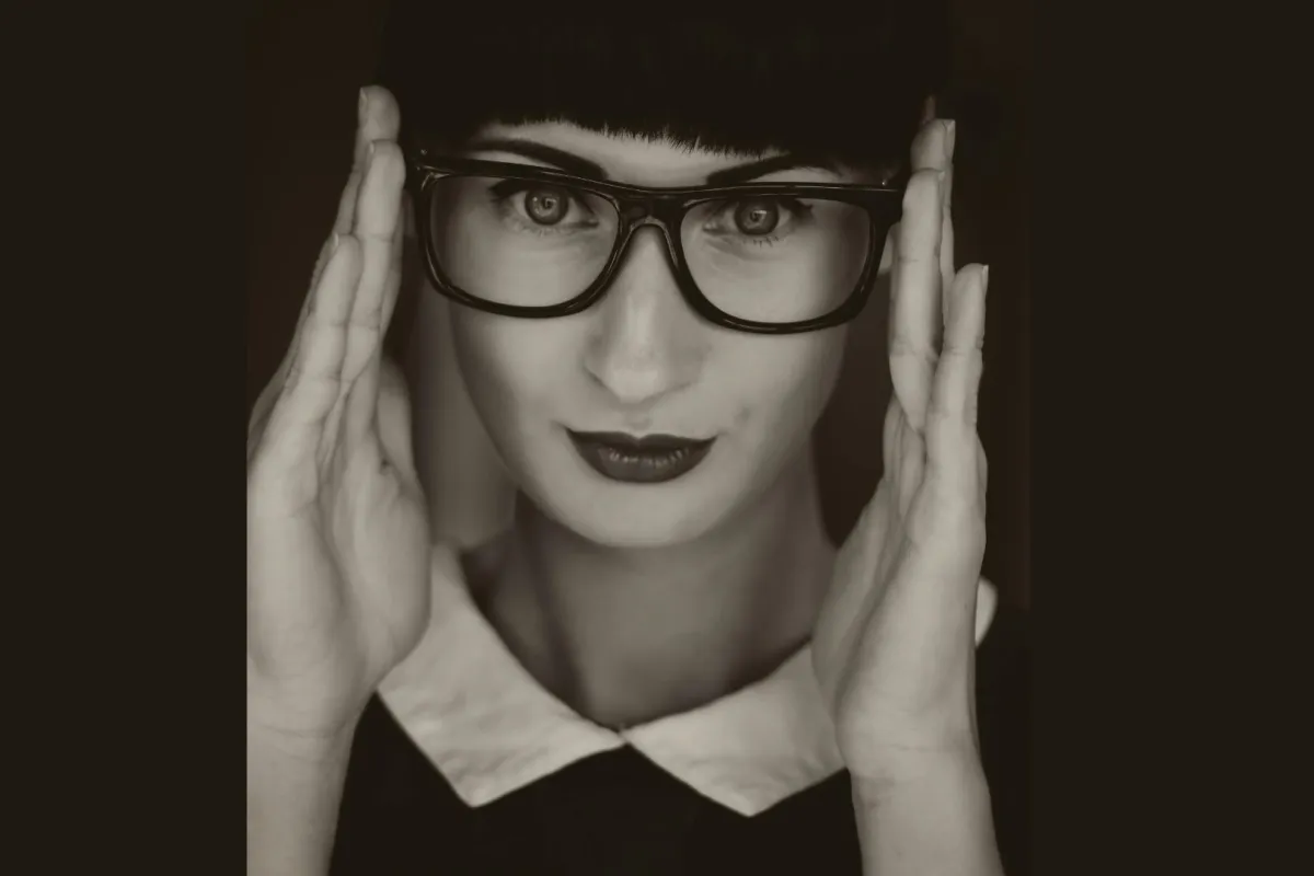 فتاة تبدو أمارات الذكاء على وجهها ترتدي نظارة وتثبتها بكلتا يديها على وجهها