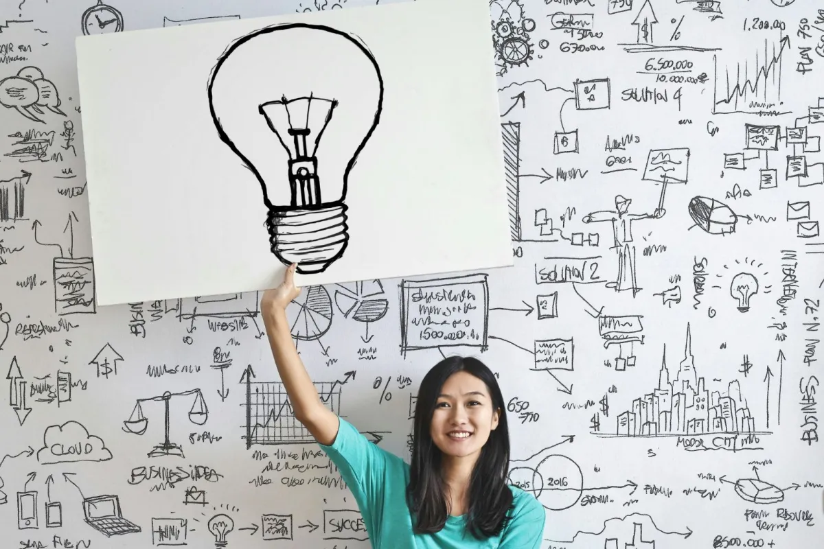 فتاة مخترعة تمسك بيدها لوحة مرسوم بها مصباح على سبورة بها مسائل حسابية كناية عن تفتح عقلها المخترع