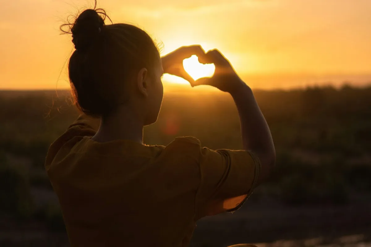 فتاة تصنع قلبًا تحتجز أشعة الشروق بكلتا يديها