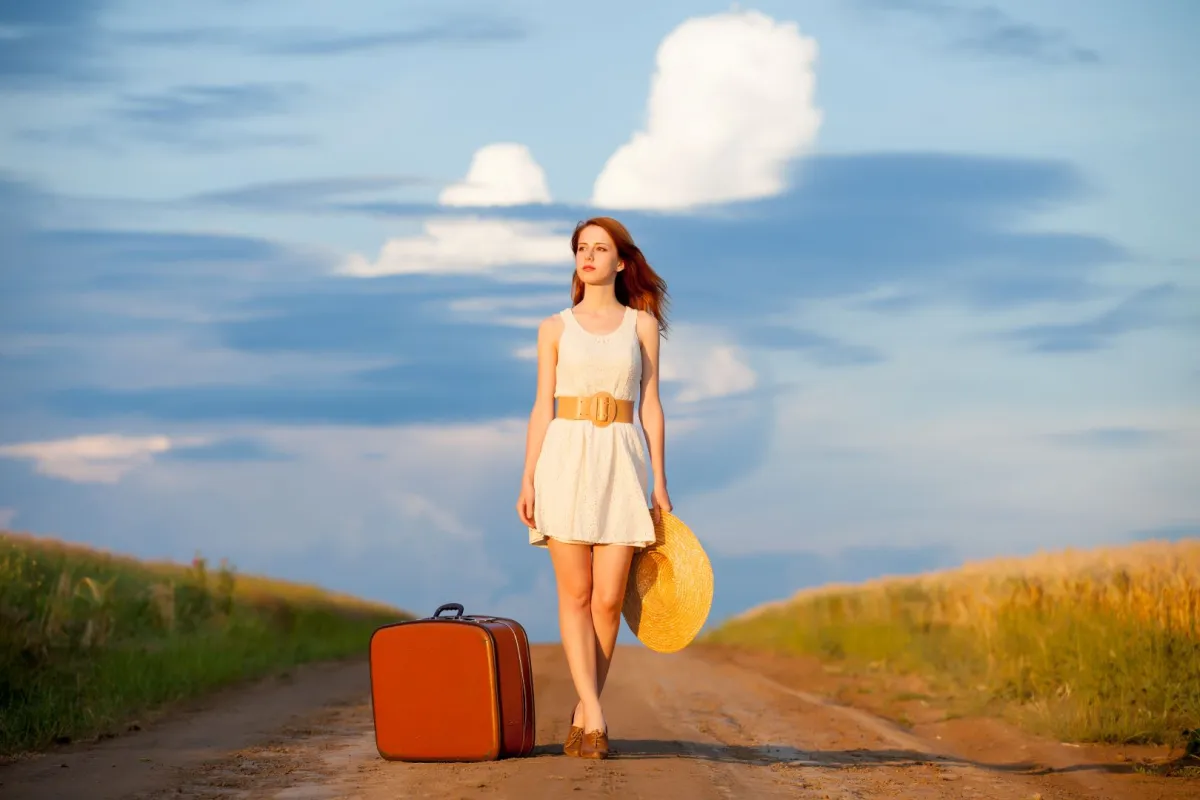 امرأة شابة جميلة تحمل قبعة وبجانبها حقيبة سفر
