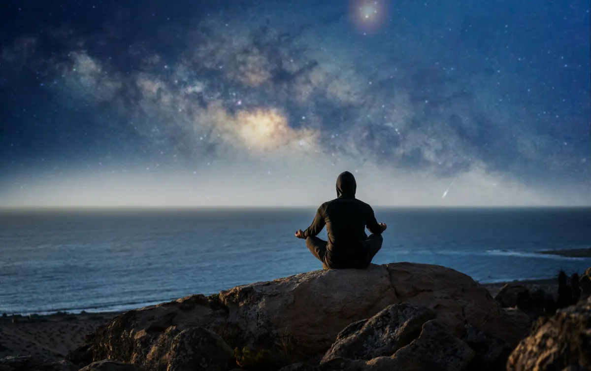 رجل يجلس على قمة الجبل ويتأمل في الليل 