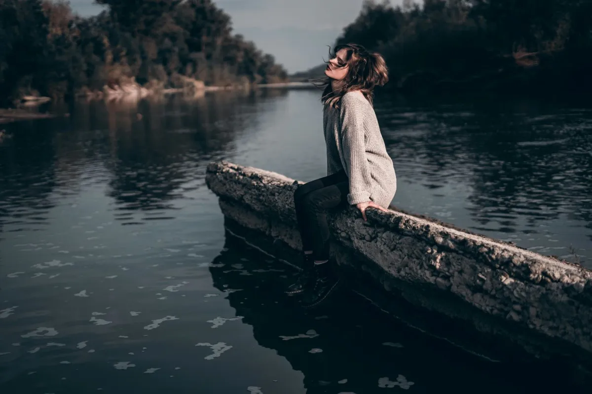 شابة تجلس في وحدة تحيط بها الطبيعة تشاركها أحزانها وعزلتها