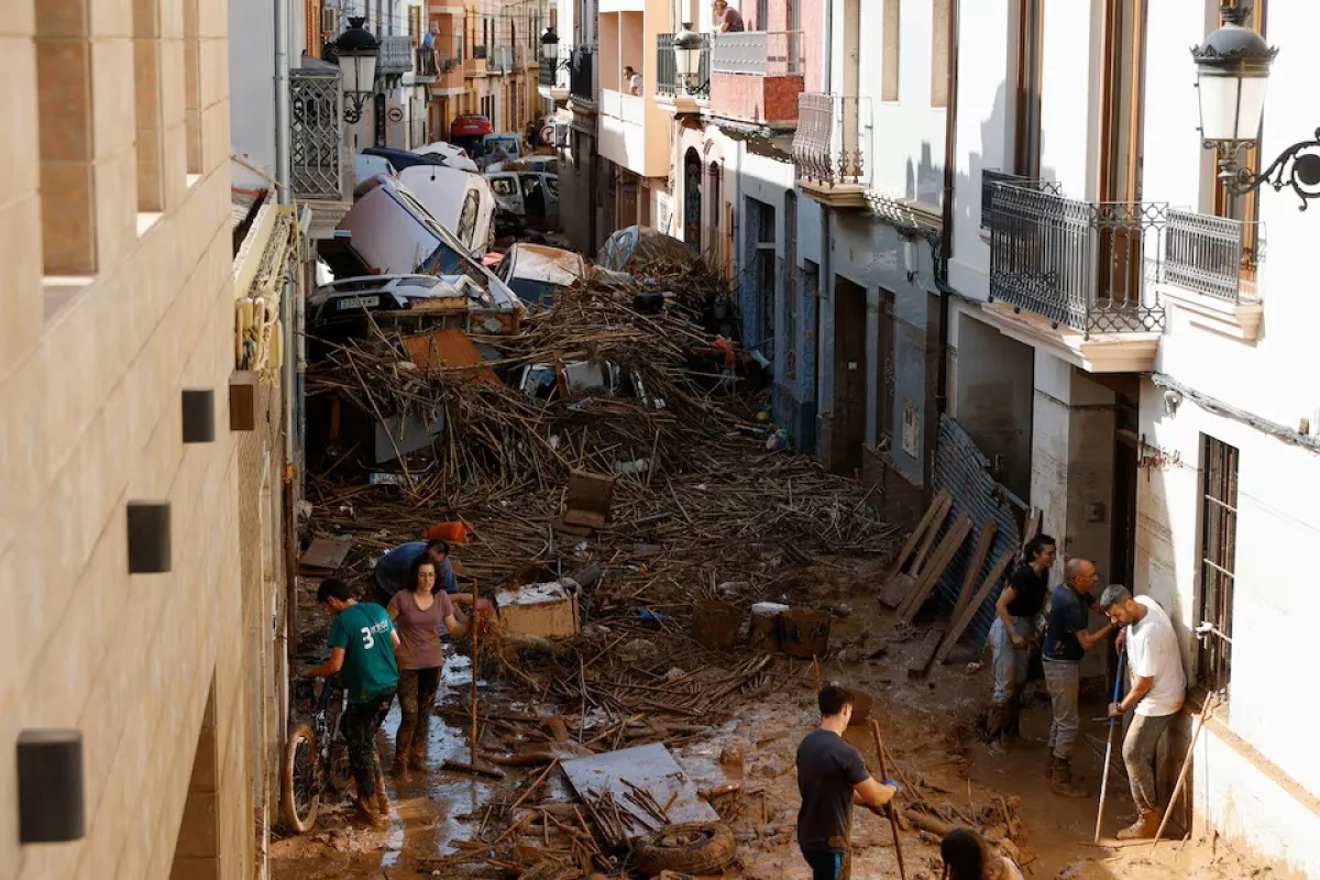 People work to clear a mud-covered street with piled up cars in the aftermath of torrential rains that caused flooding, in Paiporta, Spain,
