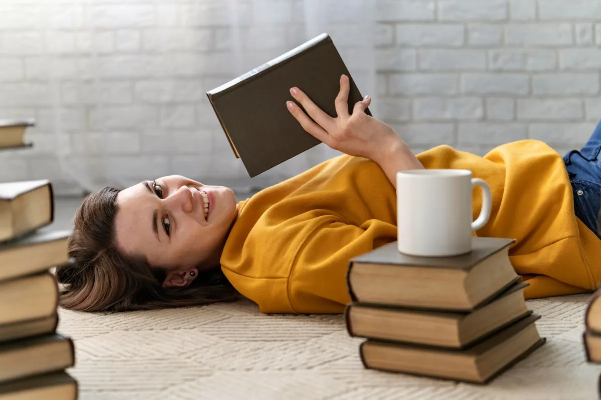 فتاة تستلقي بمرح يحيط بها مجموعة من الكتب