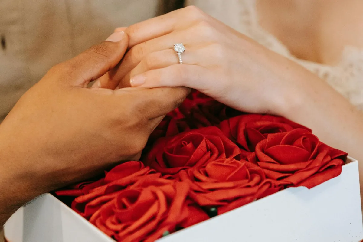 خطيب يمسك بيد خطيبته ويظهر خاتم الخطبة الماسي فوق باقة من الزهور الحمراء
