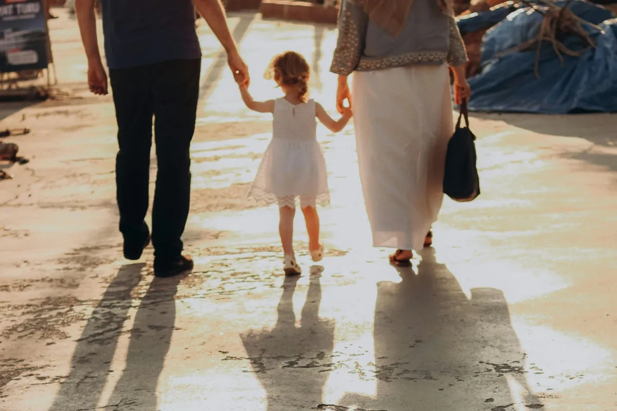 زوج وزوجه يمسكان بيد صغيرهما ويتنزهان في ضوء الشمس 