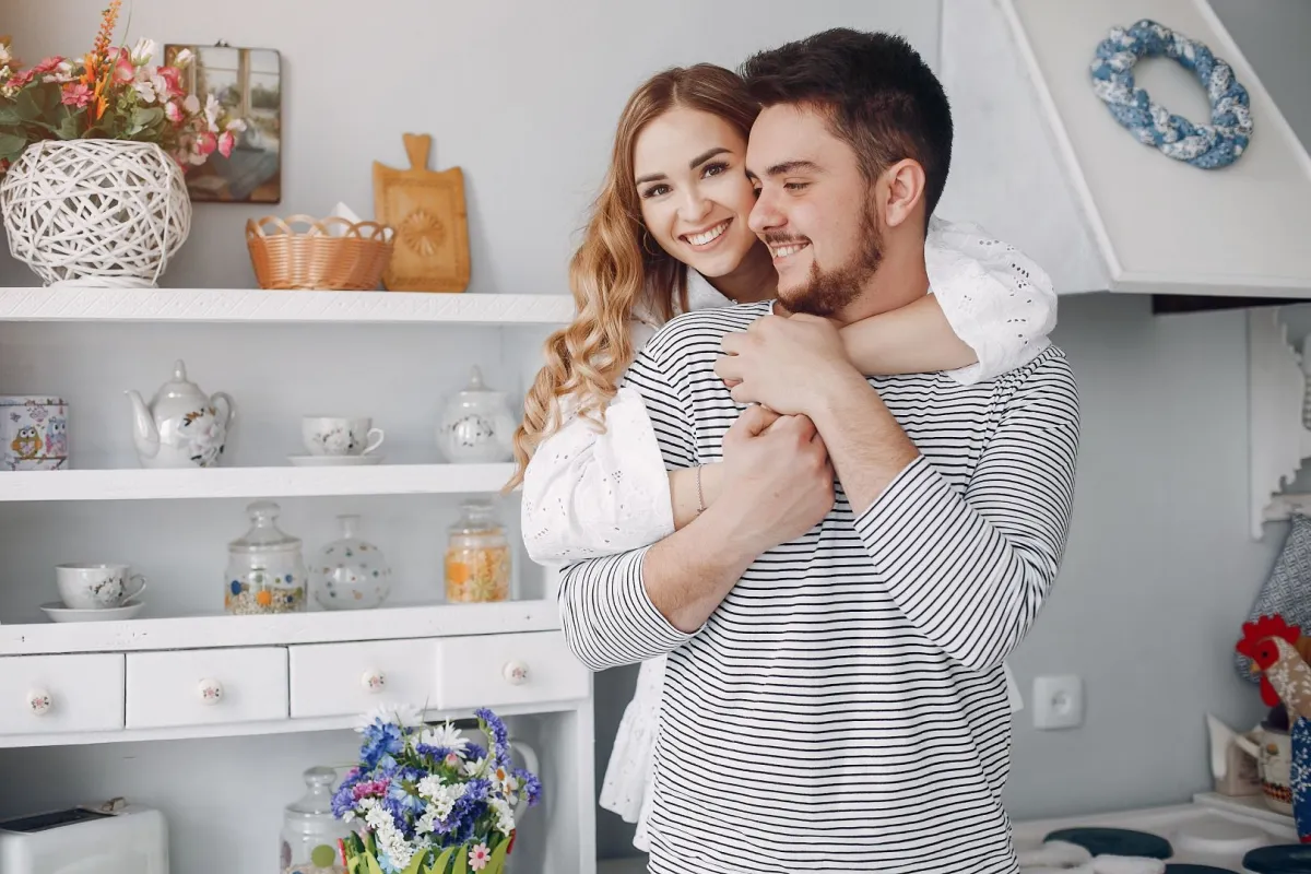 زوجة تحتضن ظهر زوجها وهو يمسك يديها وهما يبتسمان 