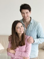 زوج يحتضن كتف زوجته ويبتسم بمحبة وهي تبتسم بسعادة   