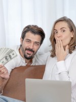 زوج يعطي زوجته مبلغاً من المال وهي سعيدة تجلس خلف اللاب توب  
