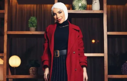 زهراء أشكناني بتنورة بليسيه طويلة ومعطف أحمر داكن مع إيشارب أبيض 