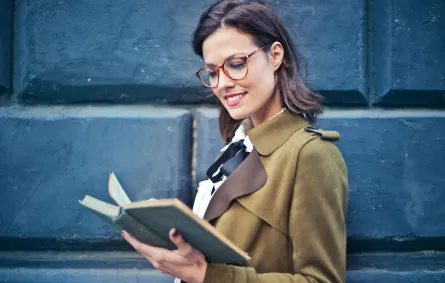 شابة ناجحة ترتدي نظارة تقرأ كتابًا تمسكه بيدها