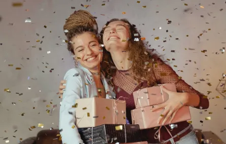 فتاة تهدي صديقتها عدداً من الهدايا وهما في قمة السعادة وتتساقط حولهما الوريقات الملونة
