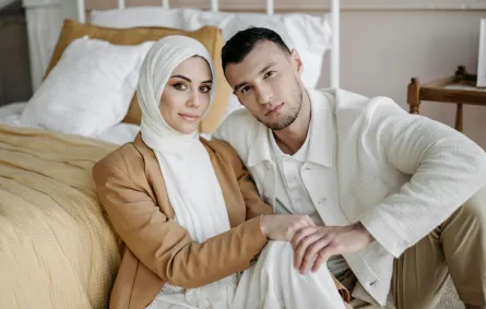 زوج يمسك يد زوجته وهما يجلسان على الأرض بجوار السرير بحجرة النوم ويبدوان سعيدين